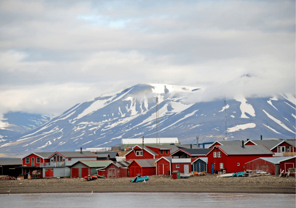 Blick vom Kreuzfahrtschiff auf die Küste von Spitzbergen mit dem Ort Longyearbyen und roten Häusern, kleinen Motorbooten und den schneebedeckten Bergen im Hintergrund